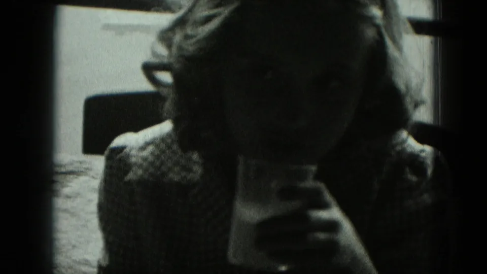A seated figure in glasses and a patterned top holds a glass near a bright window, with the face mostly in shadow in 1951 Germany footage.