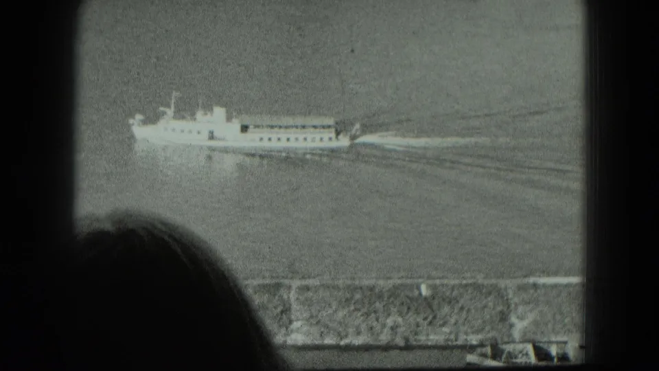 Passenger vessel on calm water in 1951 West Germany footage, with a foreground silhouette and stone wall framing the view.