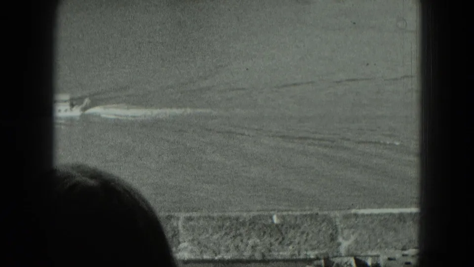 1951 West Germany home-movie view through a dark window frame toward a riverbank, open land, and a head silhouette at lower left.