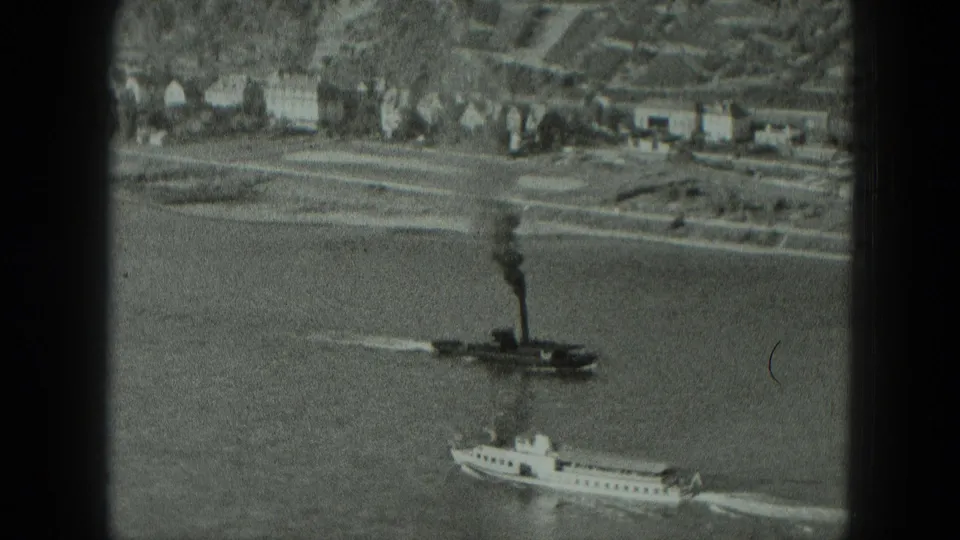 1951 West Germany river view with boats leaving wakes below shoreline houses, a stone embankment, and dark window framing.