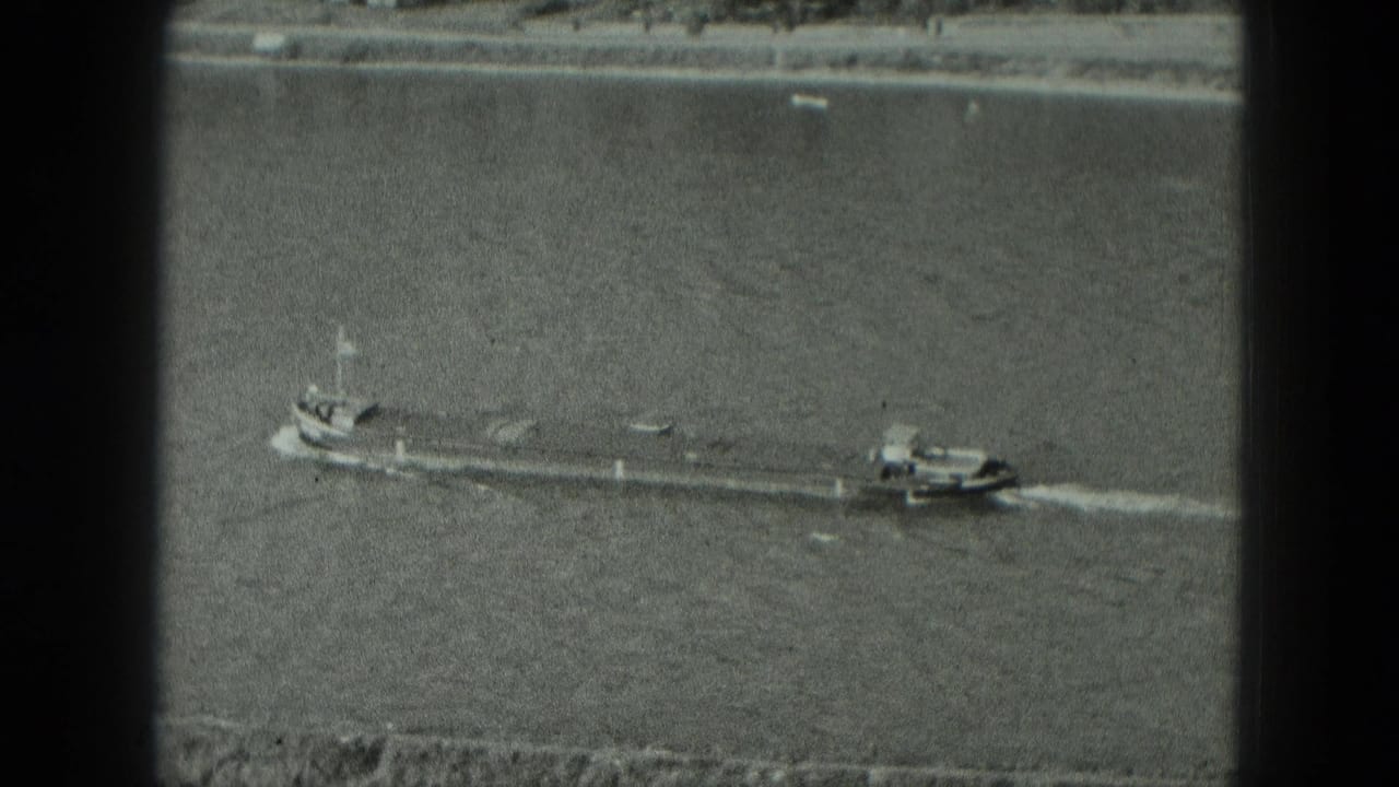 Black-and-white 8mm frame showing a long barge and small towboat on a broad German river in 1951.
