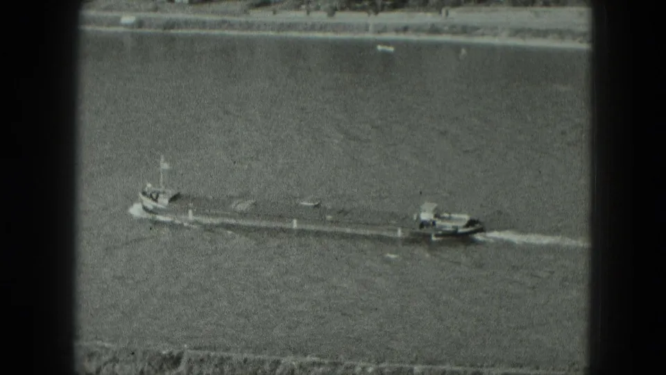 Black-and-white 8mm frame showing a long barge and small towboat on a broad German river in 1951.