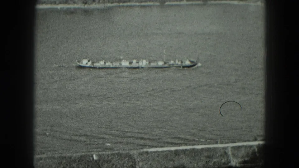 1951 Germany 8mm frame showing a long cargo vessel moving across open water below a faint shoreline.