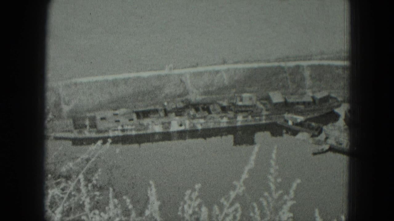 1951 West Germany riverside view with a long moored vessel, smaller boats, a pale bank, and soft film grain.