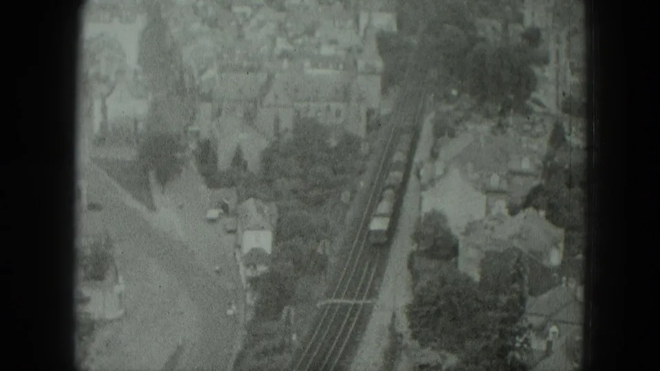 Elevated 8mm frame from 1951 West Germany showing train cars on tracks amid a residential town setting.