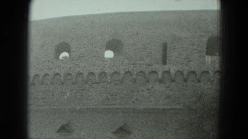 1951 West Germany home-movie frame showing a weathered stone fortress wall with arched windows and a crenellated edge.