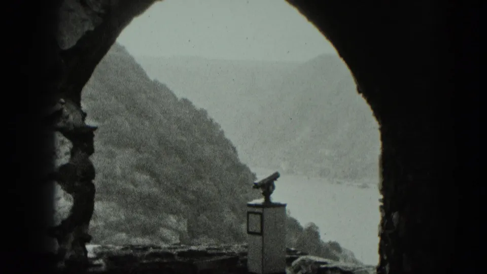 Stone archway frames a river valley in West Germany, with a coin-operated binocular viewer near the overlook.