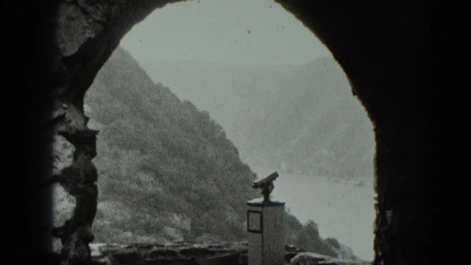 Visitor viewpoint through a fortress arch toward a river valley, with a mounted viewing binocular in the foreground.