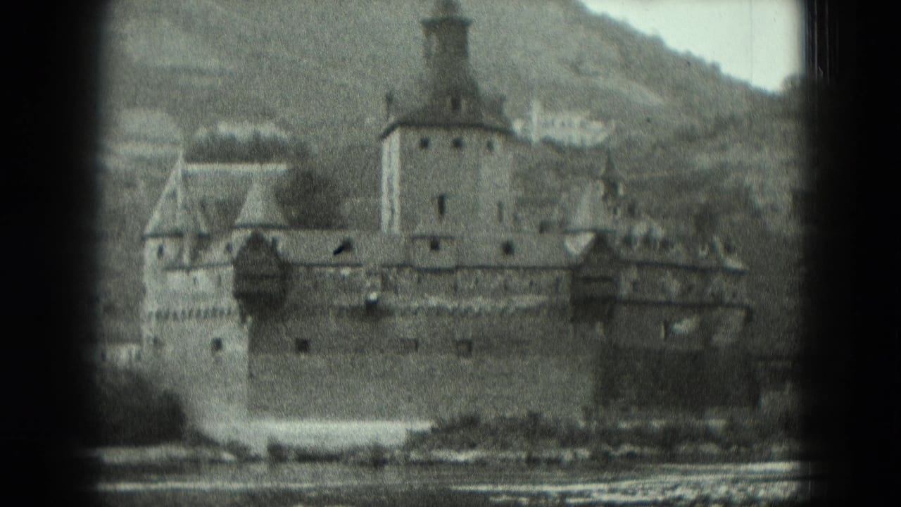 Riverside fortress seen across water, with towers, wall, hillside, and shoreline.