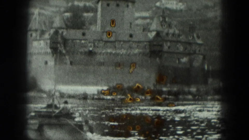 1951 8mm frame of a German riverbank with a stone castle or fortress rising close to the water.