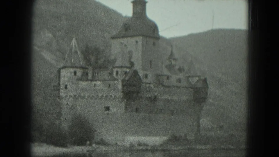 Black-and-white 1951 8mm view of a castle-like riverside structure in Germany, framed by dark gate edges and hills.
