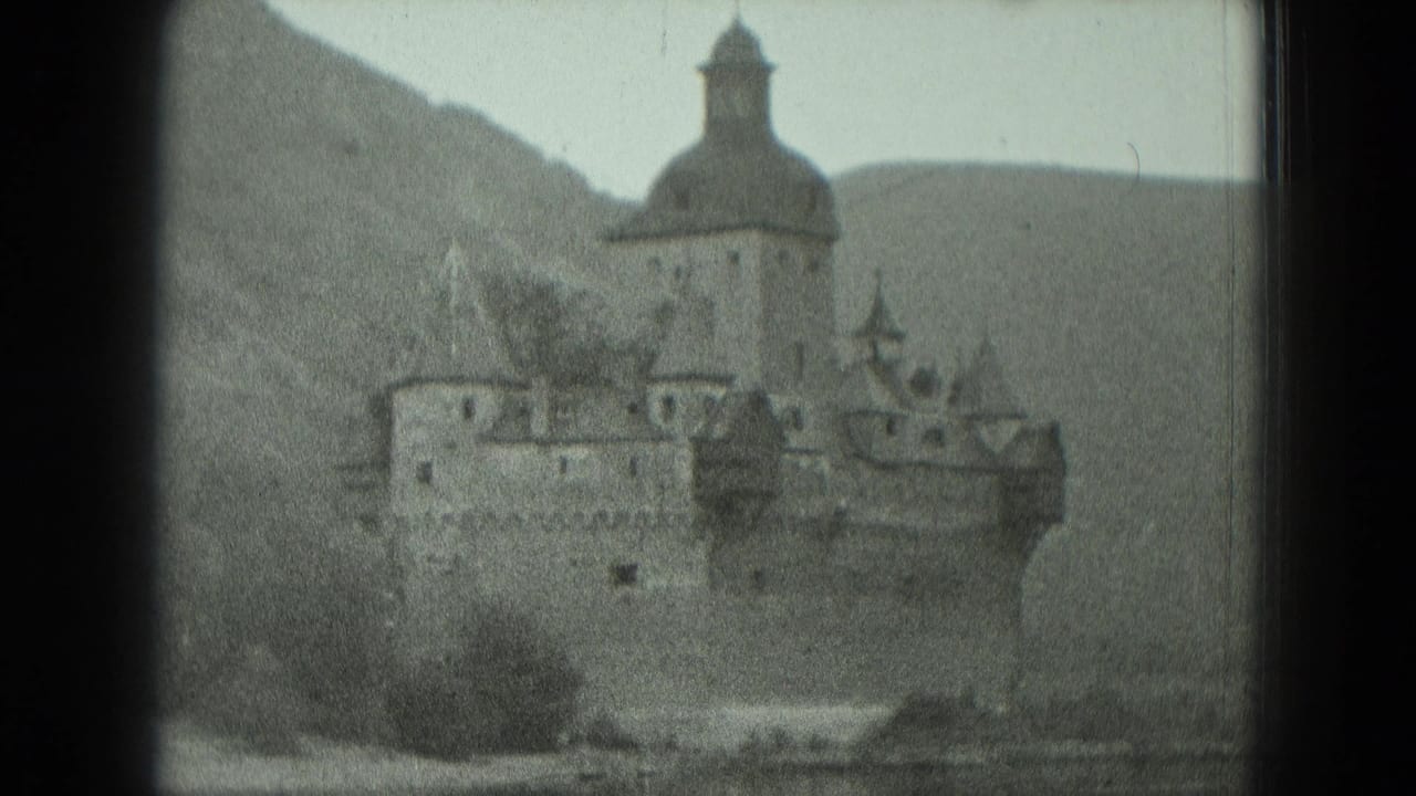 Hilltop stone castle with tower and walls seen in grainy black-and-white footage.