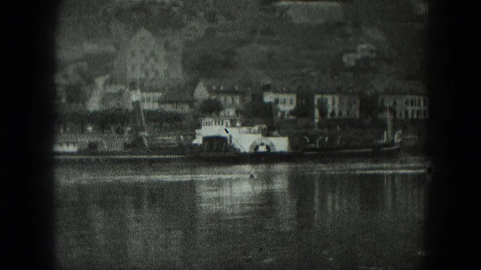 1951 West Germany riverfront view with clustered buildings, hillside backdrop, reflections, and a paddlewheel-style boat near shore.