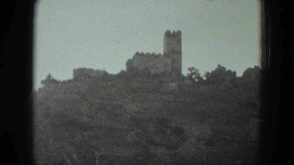 1951 West Germany home-movie frame showing a distant hilltop castle or ruin silhouetted above dark trees.
