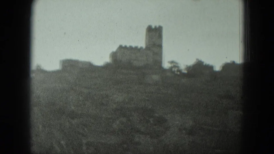Soft 8mm view of a hilltop castle or ruin in Germany, framed from a distance with trees along the ridge.