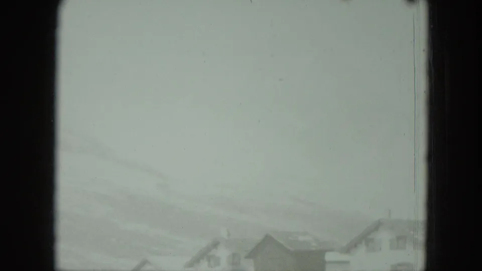 1951 Germany home-movie view of distant rooftops below a soft, snow-dusted mountain slope.