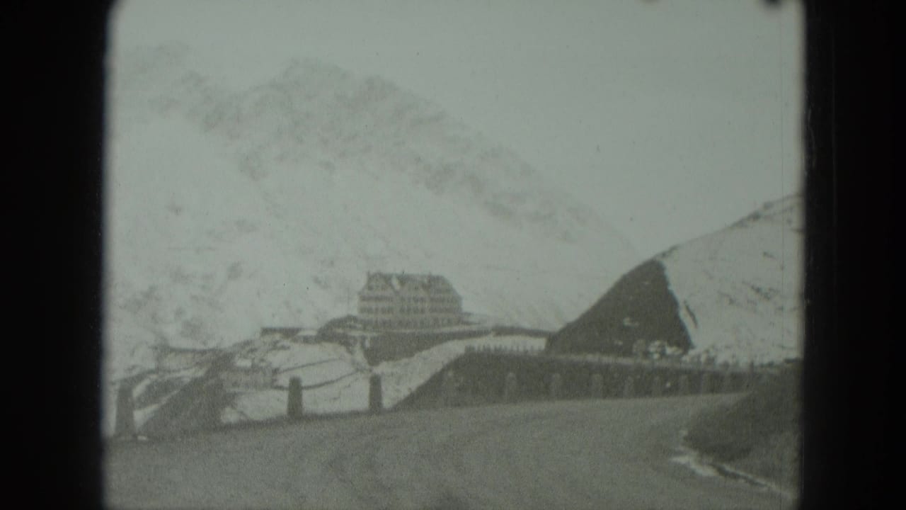 Large building and snow-covered slope viewed beyond a curving mountain road.