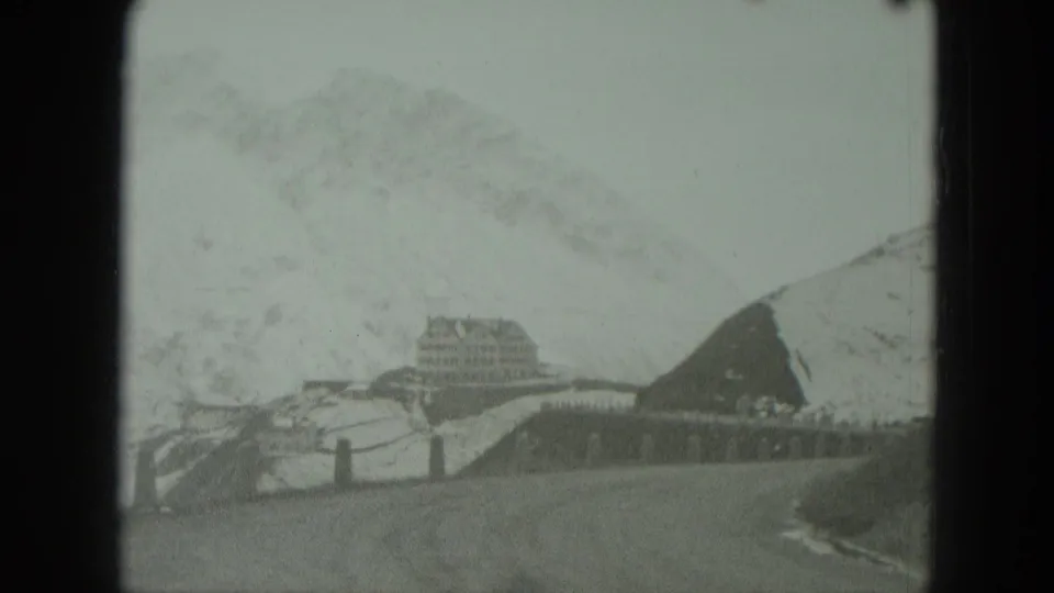 Snowy German mountain landscape with a distant lodge-like building, road posts, and soft 8mm frame edges.