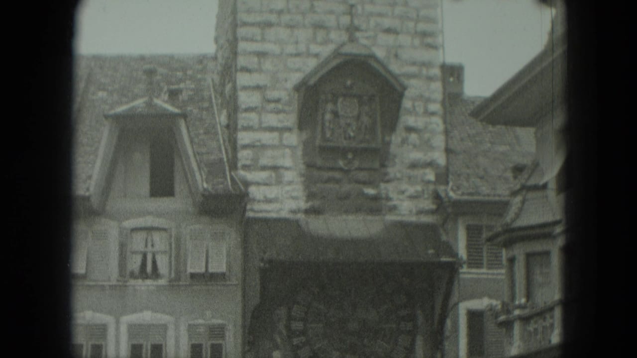 Stone clocktower and steep-roofed buildings fill the frame.