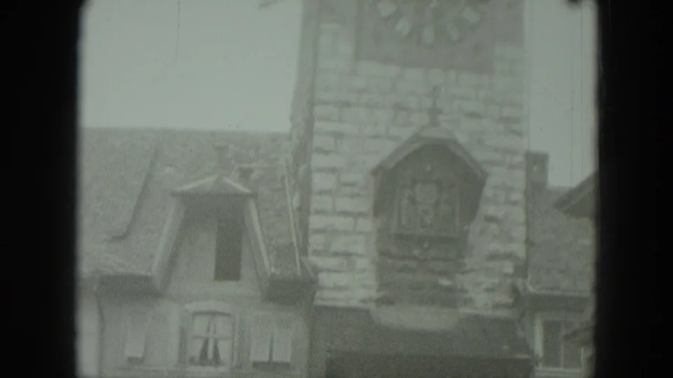 The camera holds on a soft 8mm view of the stone tower, dormer windows, and steep roofs in a German town setting.