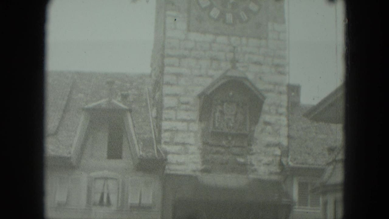 Stone clock tower with large clock face and cuckoo-clock structure above rooftops.