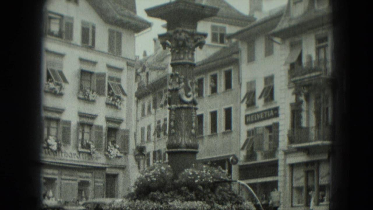 Ornate fountain column stands among shuttered buildings and shopfronts in a town square.