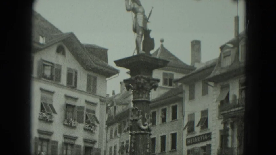 1951 West Germany home-movie frame showing a statue above an ornate fountain in a historic town square setting.