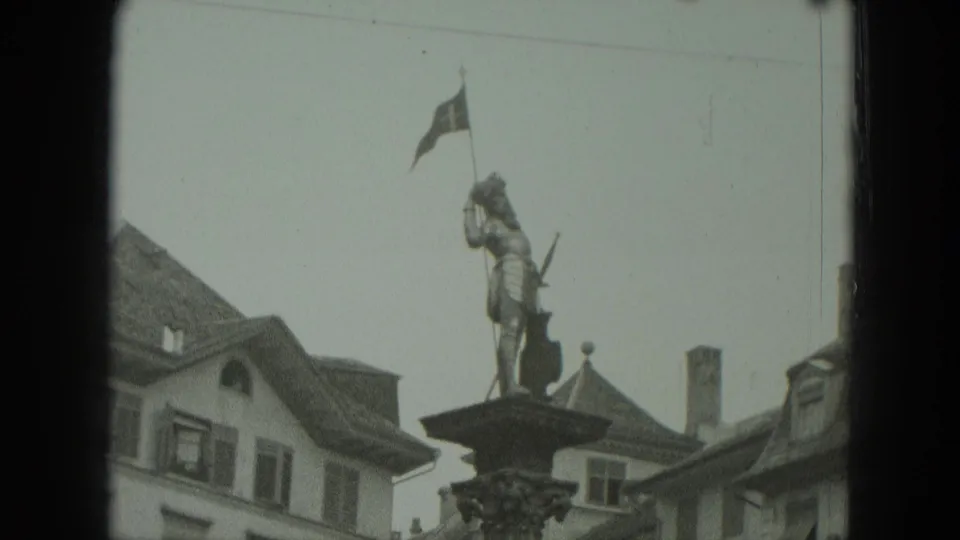 1951 West Germany 8mm view of the statue and column, with shuttered windows and older rooflines filling the background.