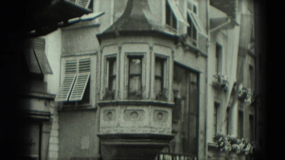 1951 Germany 8mm frame showing an older urban building facade with a projecting bay window, louvered shutters, and flower boxes.