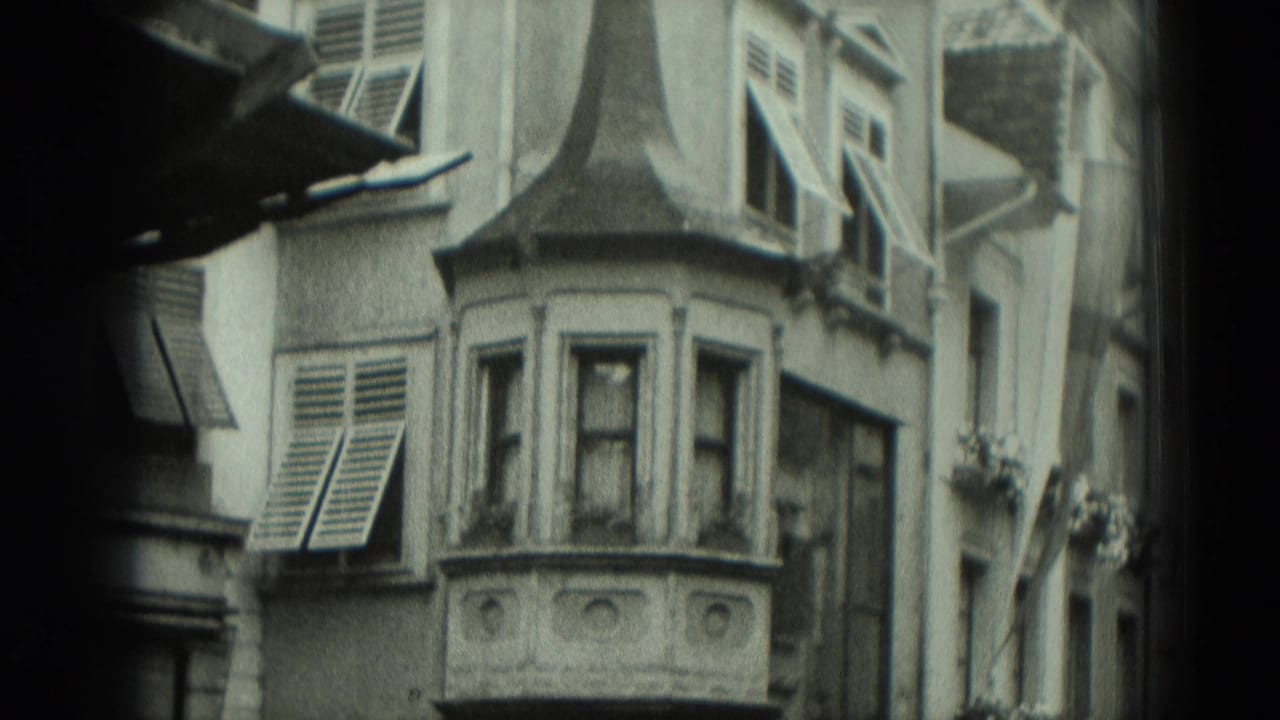 1951 Germany 8mm frame of an older facade with shuttered windows, decorative bay projection, and flower boxes along the street side.