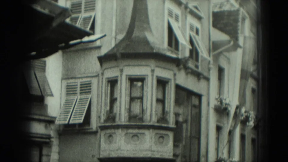1951 Germany 8mm frame of an older facade with shuttered windows, decorative bay projection, and flower boxes along the street side.