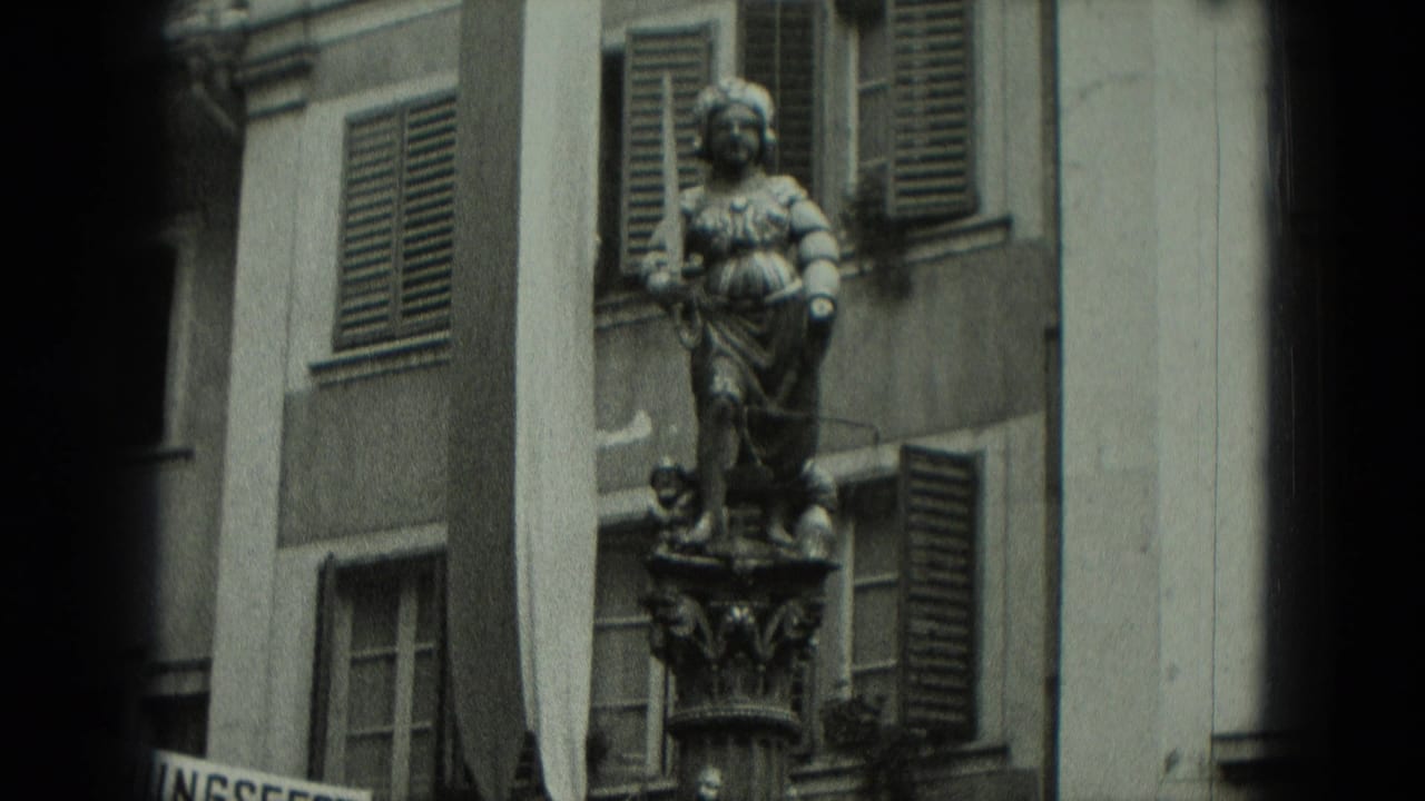 Stone robed figure on an ornate pedestal beside shuttered windows.