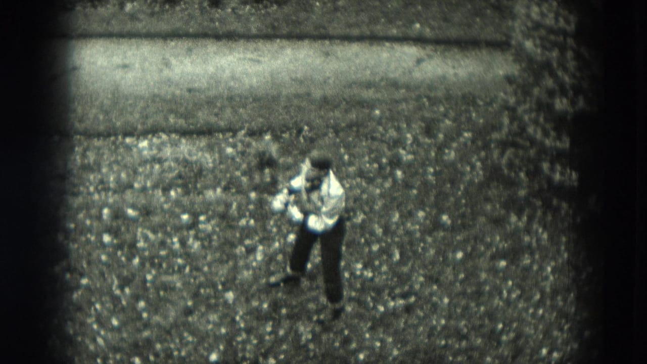 High-angle 1951 West Germany 8mm frame of a boy in a light shirt and dark pants standing alone on gravel during outdoor play.