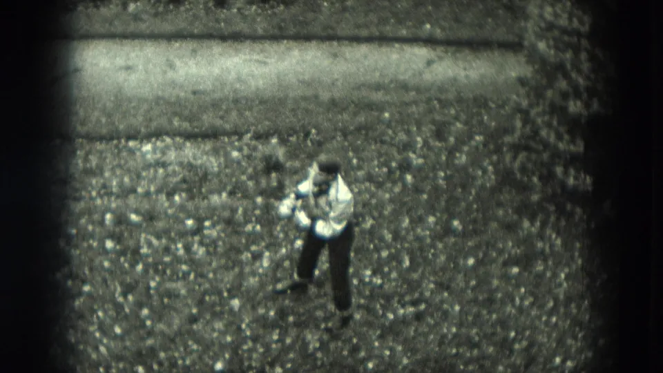 High-angle 1951 West Germany 8mm frame of a boy in a light shirt and dark pants standing alone on gravel during outdoor play.