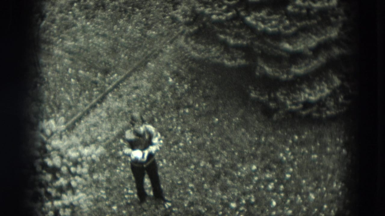 High-angle 8mm frame shows the boy on a gravel yard near planted edging, with soft focus and dark film borders.