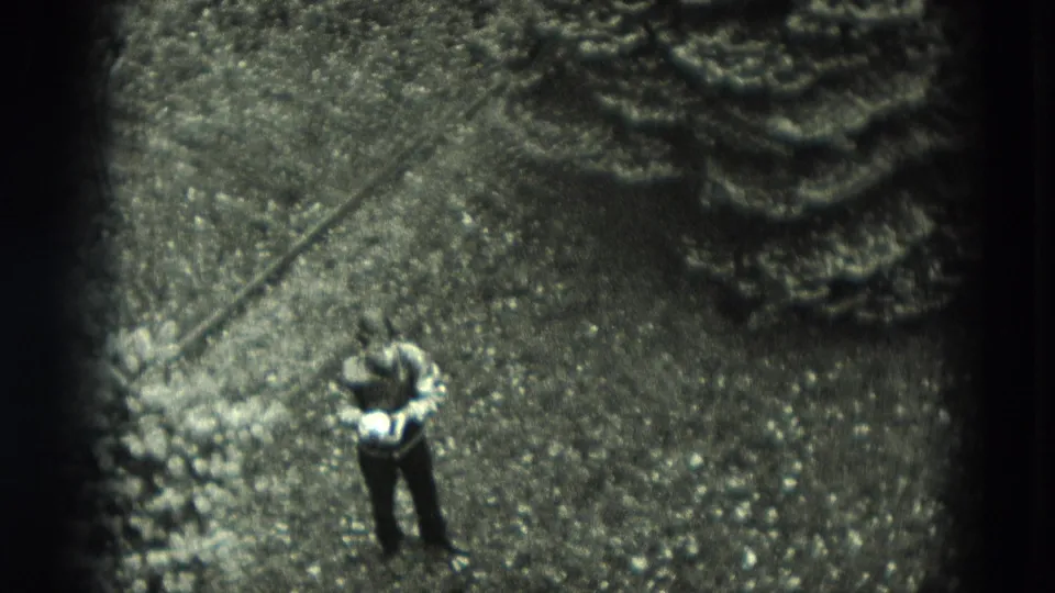 High-angle 8mm frame shows the boy on a gravel yard near planted edging, with soft focus and dark film borders.