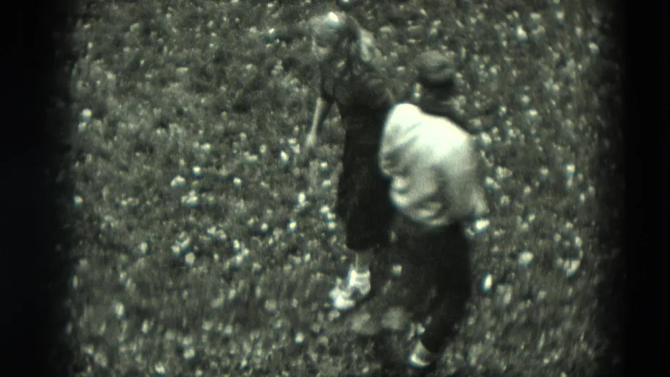 The boy bends forward near the girl as they play on grass in the supplied 1951 Germany home-movie footage.