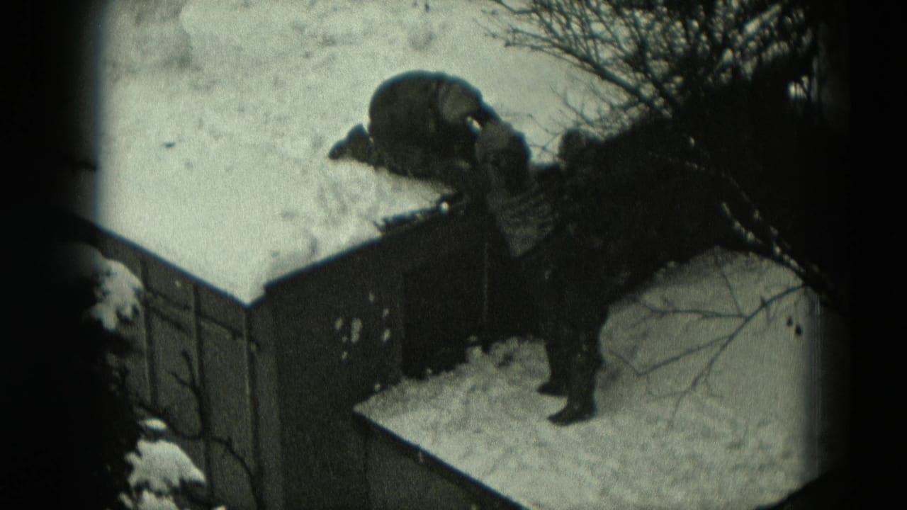 Two bundled figures around a snow-covered roof, one kneeling above while another reaches up from below.