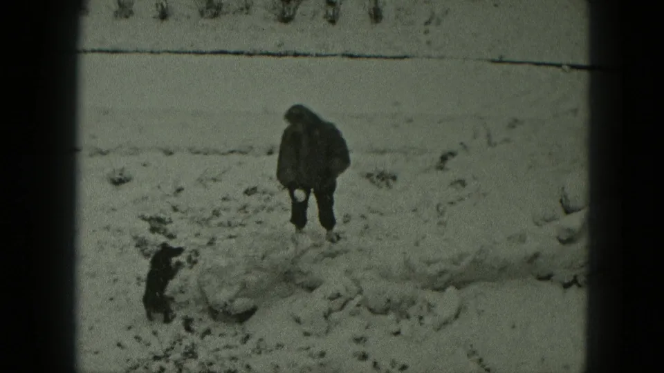 A bundled person and small dog face one another in a snowy field, captured in 1951 West Germany home-movie footage.
