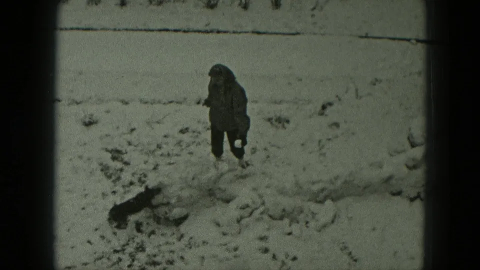 In 1951 West Germany home-movie footage, a bundled person stands in snow while a small dark dog moves nearby.