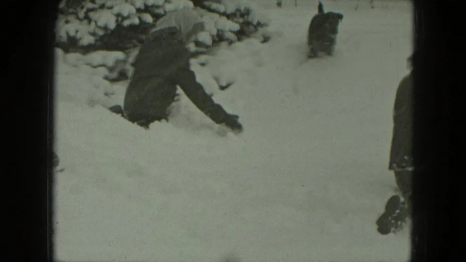 In 1951 Germany home-movie footage, a bundled woman crouches in a snowy yard as a small dark dog approaches.