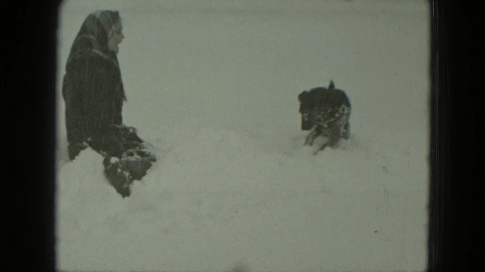 The 8mm frame shows a bundled woman at left and a small dark dog facing her across deep snow.