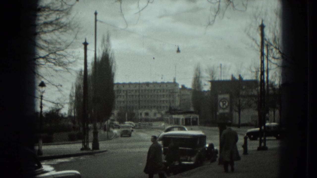 Tree-lined city boulevard with cars, pedestrians, street lamps, and distant buildings.