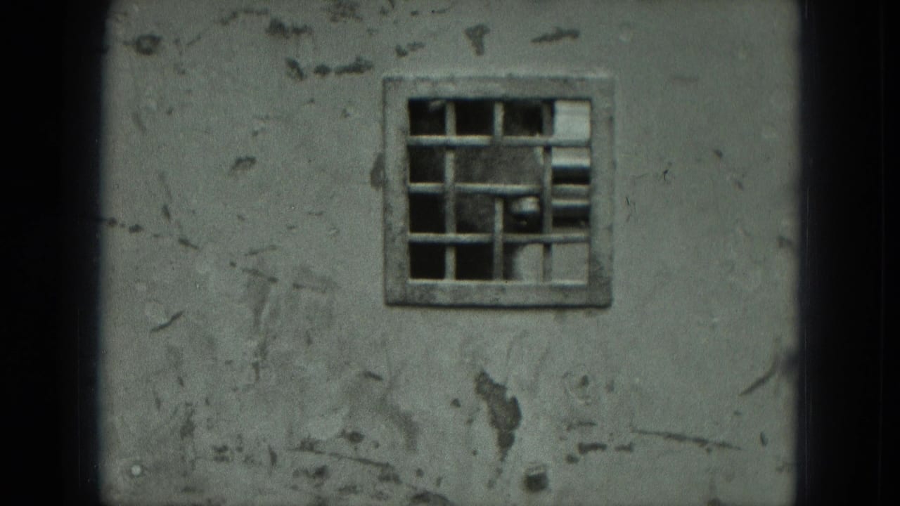 Close view of a worn cement wall in Germany with peeling surface marks and a small barred window set high in the frame.