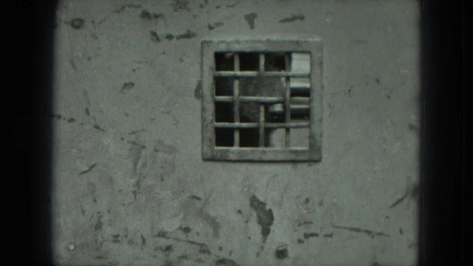 Close view of a worn cement wall in Germany with peeling surface marks and a small barred window set high in the frame.