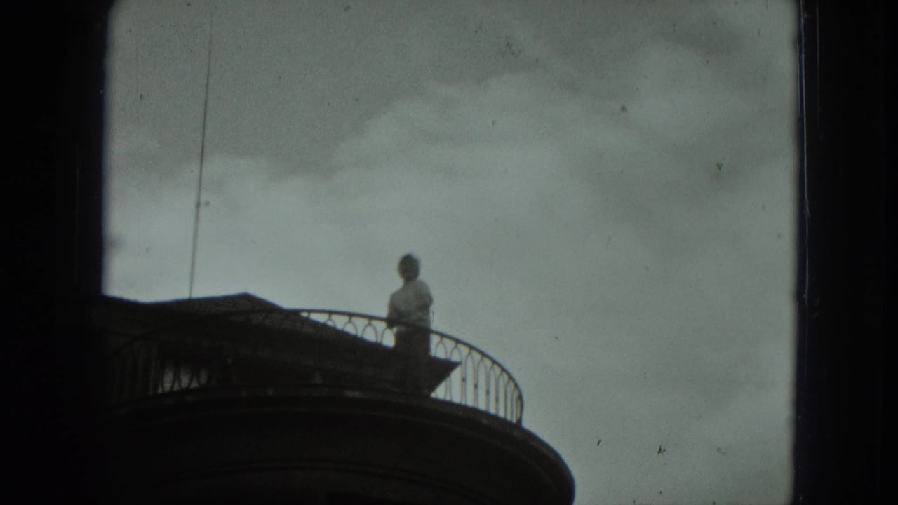 A distant person stands on a curved balcony against a cloudy sky.