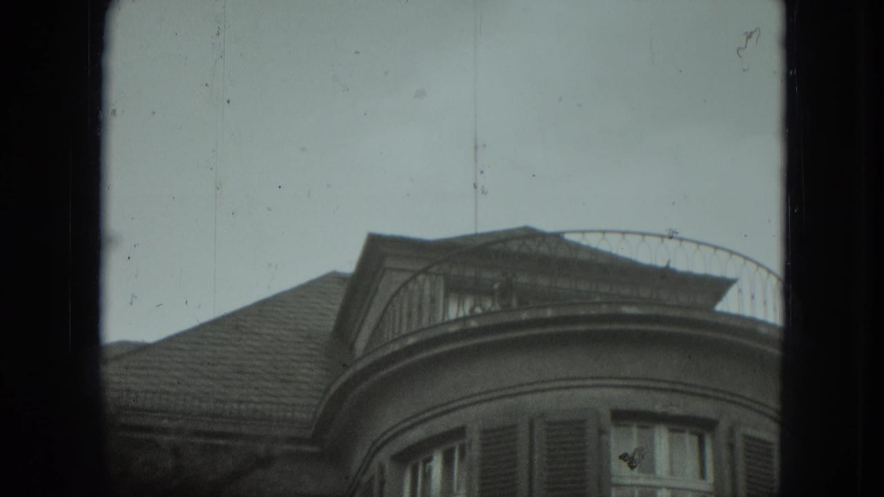 A low-angle 8mm view shows the curved balcony, shuttered windows, and roofline of a West Germany residence.