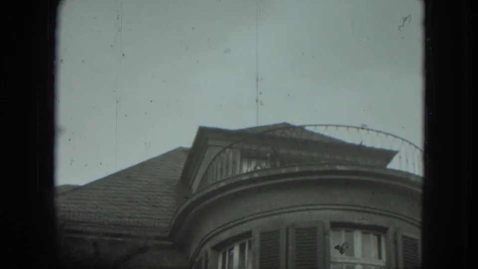 A low-angle 8mm view shows the curved balcony, shuttered windows, and roofline of a West Germany residence.