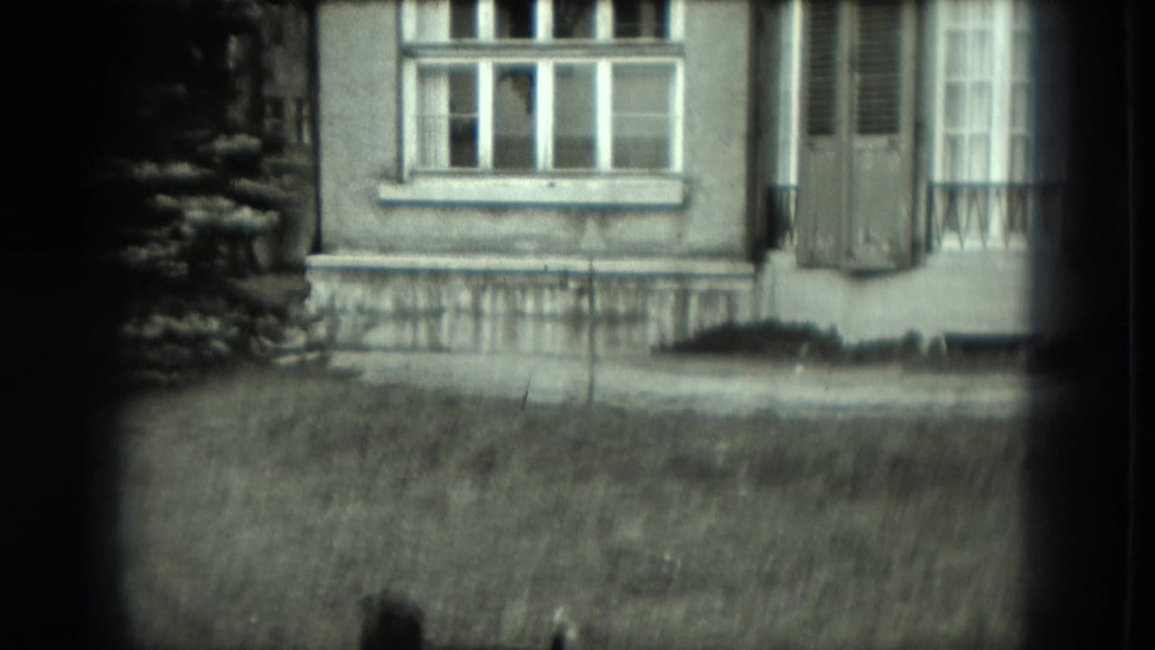House facade with windows and a lawn, partly obscured by dark film edges.
