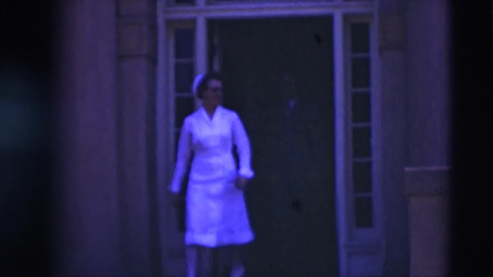 In 1951 Paducah footage, a woman in a white nurse-style uniform exits a shaded building entrance into daylight.